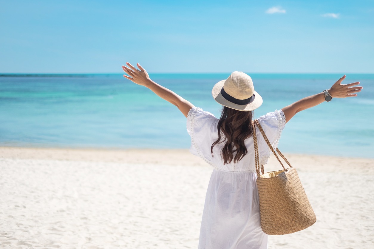 A woman on a beach with a beach tote on her shoulder