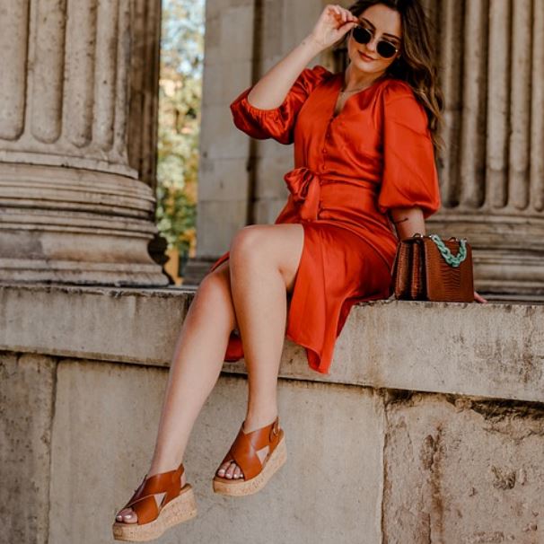 a woman sitting on a high place wearing jute wedges with her bag next to her